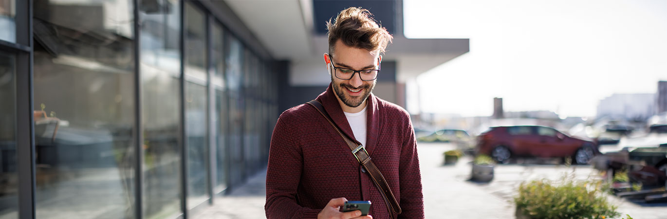 Mann steht vor einem Gebäude und lächelt während er auf sein Handy schaut